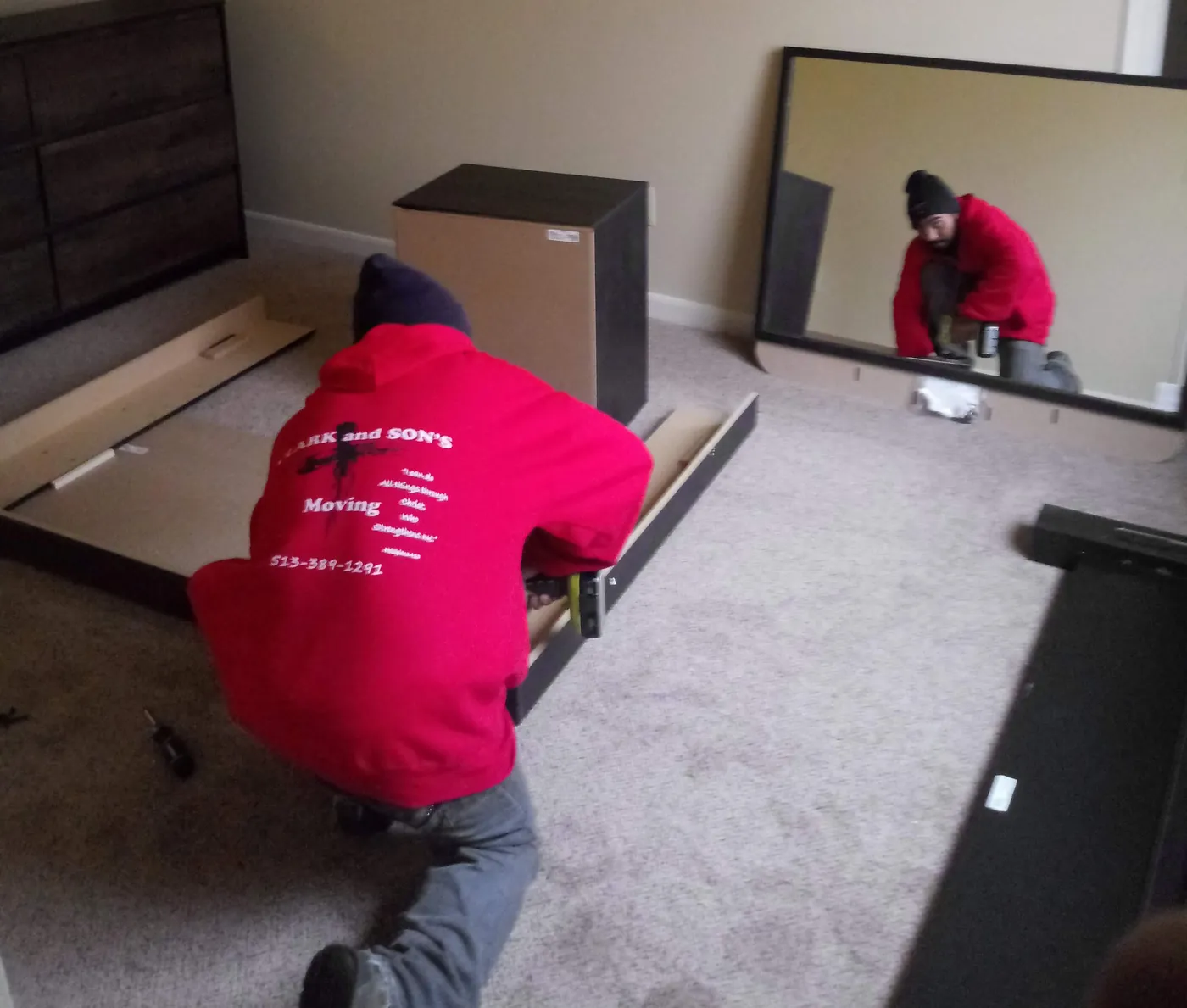 Two movers putting a bed frame back together in a new bedroom