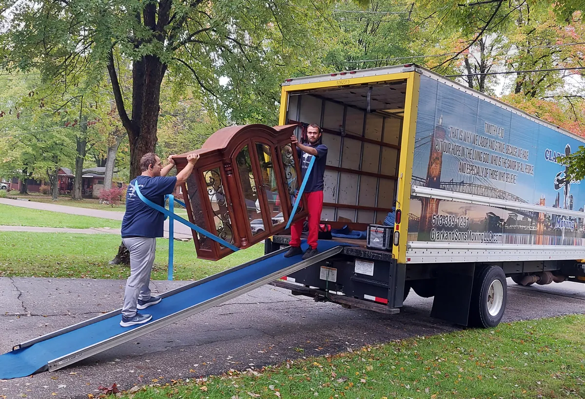 Two movers walking a wooden hutch down the ramp of a Clark and Sons truck