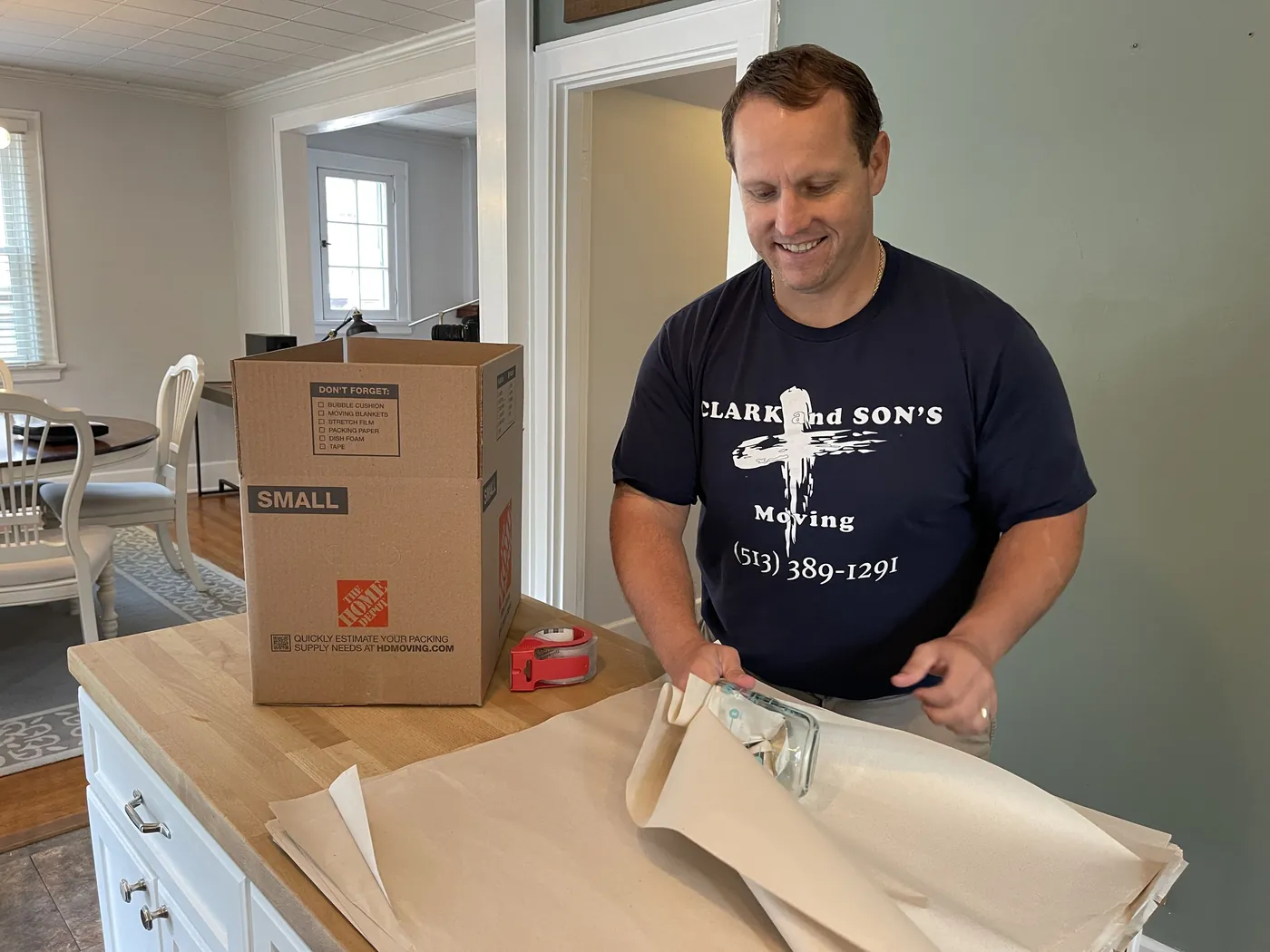 Clark and Sons mover wrapping dishes in packing paper at a kitchen counter