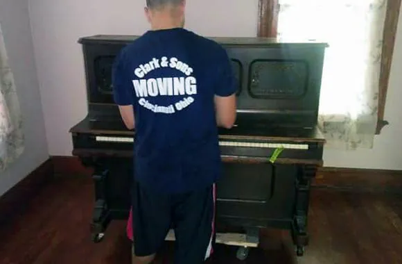 Clark and Sons mover in a company shirt rolling an upright piano