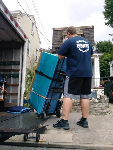 Clark and Sons mover rolling a teal gun safe up a truck ramp on a heavy dolly