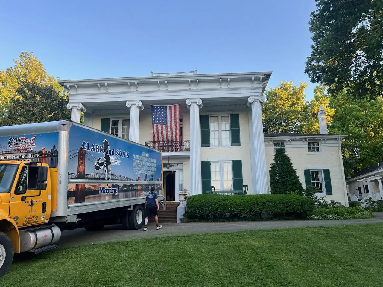 A Clark and Sons truck parked in front of a white-columned house with an American flag